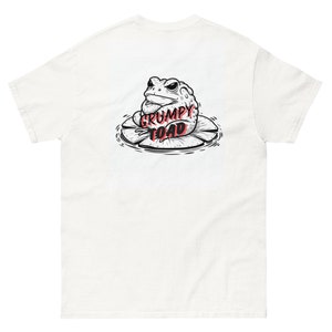 May include: White t-shirt featuring a black and white illustration of a grumpy toad sitting on a lily pad. The text "GRUMPY TOAD" is written in red.