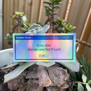 May include: A holographic sticker with a blue, pink, and green gradient. The sticker features a system error message that reads "Error 404: Gender.exe Not Found" with an "OK" button.