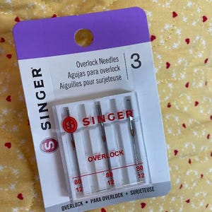 May include: A package of Singer overlock needles. The package is white and purple, with the Singer logo and the word "OVERLOCK" printed on it. The package contains three needles, size 80/12.
