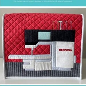May include: Red quilted serger cover with a geometric design. The cover features a black pocket, a white panel with "BERNINA" in red, and a gray base. The cover is designed for the BERNINA L Series of overlockers.
