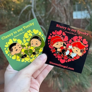 Puede incluir: Dos juegos de pines esmaltados. Un juego presenta dos figuras de dibujos animados en una tarjeta verde con el texto "Clancy to my Torchy". El otro juego presenta dos figuras en una tarjeta negra con el texto "Blurry to my Spooky" y el sitio web bluewolfangel.com.