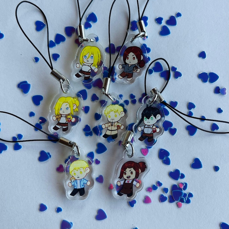 Op de afbeelding: Set van acht kleurrijke anime-personagecharms met een zwarte koord eraan bevestigd. De charms zijn gemaakt van helder acryl en tonen verschillende personages met verschillende gezichtsuitdrukkingen.