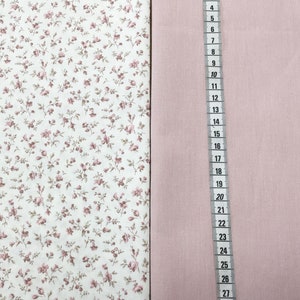 Könnte beinhalten: Zwei Stoffmuster. Eines hat einen weißen Hintergrund mit einem Muster aus kleinen rosa und braunen Blumen. Das andere ist ein einfarbiger, hellrosa Stoff. Ein Lineal wird neben dem rosa Stoff platziert, mit Messungen in Zentimetern.