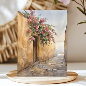 May include: A watercolour painting depicting a narrow stone alleyway leading towards the sea. A tall, weathered tan wall features a dark wooden doorway adorned with vibrant pink bougainvillea flowers cascading from above.