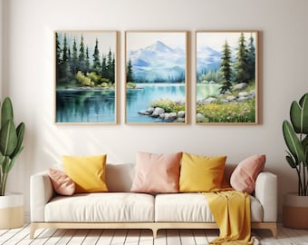 May include: A triptych of framed wall art prints featuring a watercolor landscape of a calm lake, dense evergreen forests, and distant blue mountains. The artwork displays rocky shorelines, patches of yellow wildflowers, and soft reflections.