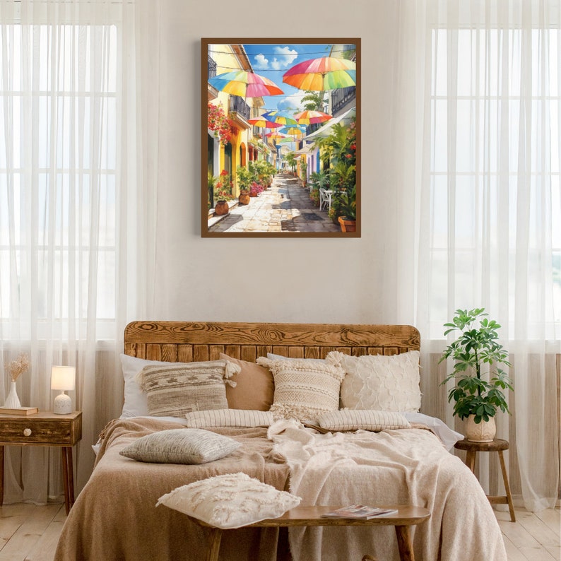 May include: A painting depicting a colourful street scene with vibrant umbrellas hanging above a cobbled street lined with buildings. The buildings are painted in shades of yellow and have green plants growing on their walls.
