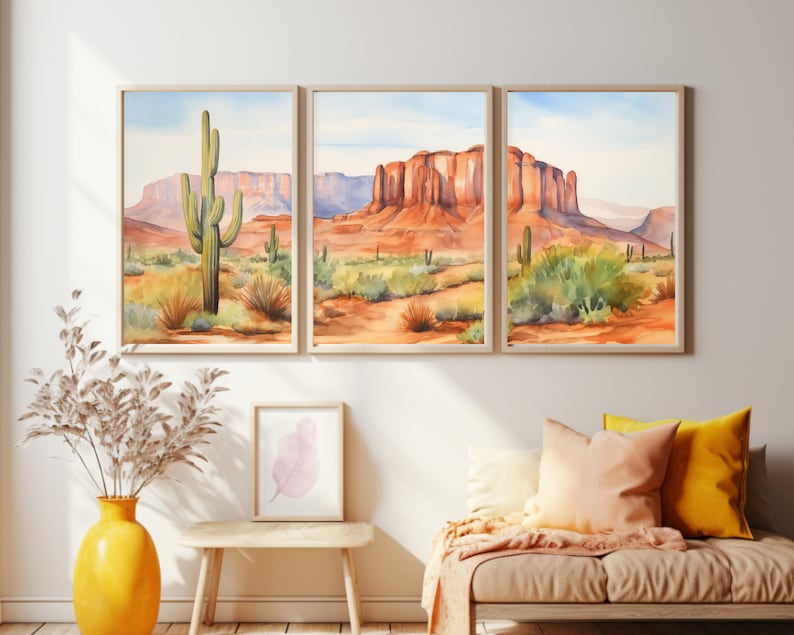 May include: A triptych of framed watercolour prints depicting a desert landscape with red rock mesas, saguaro cacti, and sparse vegetation under a pale blue sky. The artwork is displayed in light wood frames on a plain wall above a seating area.