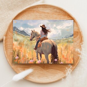 May include: An art print showing a person on horseback in a field of wildflowers. The rider wears a cowboy hat and a light-coloured shirt. The horse is light grey, and the background features mountains and a cloudy sky. The colour palette includes soft blues, greens, and oranges.