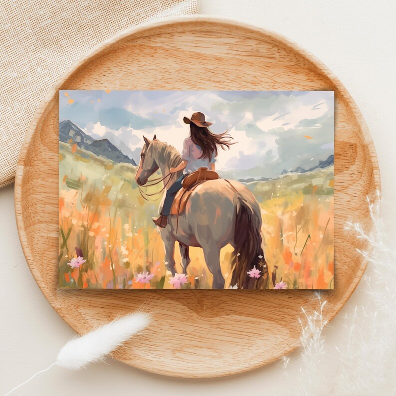May include: An art print showing a person on horseback in a field of wildflowers. The rider wears a cowboy hat and a light-coloured shirt. The horse is light grey, and the background features mountains and a cloudy sky. The colour palette includes soft blues, greens, and oranges.