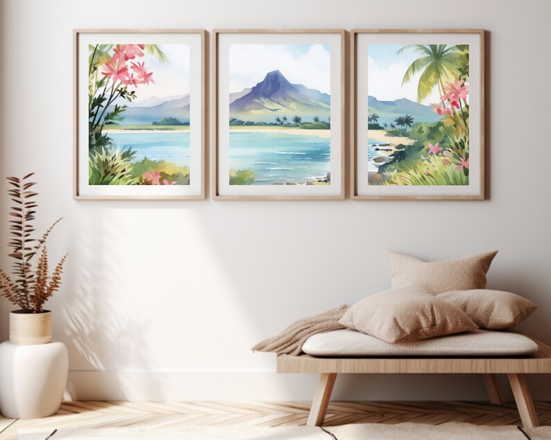 May include: A set of three framed wall art prints featuring watercolour tropical landscapes. Each print displays a coastal scene with blue water, sandy beaches, green palm trees, and pink flowers, with a central mountain peak in the middle frame.
