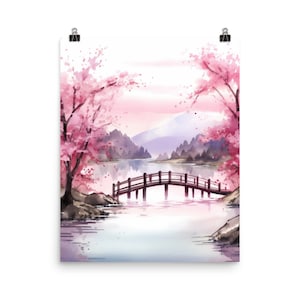 May include: A watercolour art print featuring a landscape with pink cherry blossom trees, a dark wooden arched bridge spanning a calm lake, and distant purple mountains under a soft light sky. The artwork is displayed with two black metal clips.