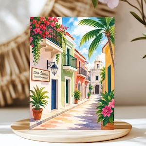 May include: A colorful painting of a street in Zona Colonial Santo Domingo featuring pastel buildings with balconies, vibrant pink bougainvillea, green potted plants, a tall palm tree, and a distant white church under a bright blue sky.
