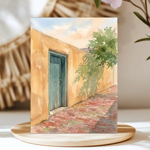 May include: A watercolor painting depicting a narrow alleyway with a textured tan wall, a weathered teal wooden door, and a red brick path. A green tree casts a soft shadow across the wall under a pale blue and orange sky.
