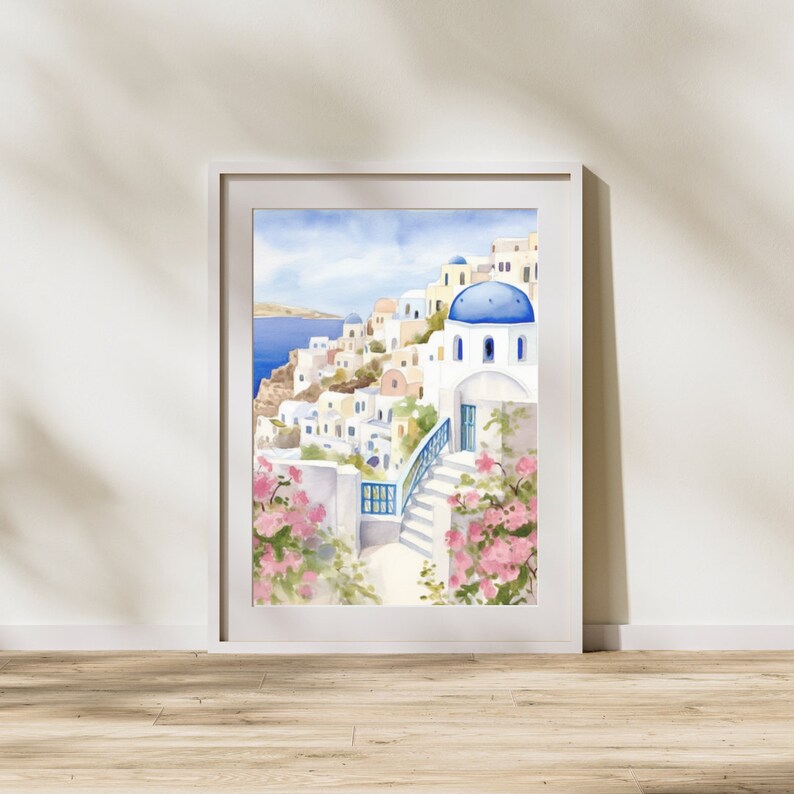 Puede incluir: Una l&aacute;mina de acuarela enmarcada que representa un pueblo costero mediterr&aacute;neo con edificios blancos, c&uacute;pulas azules y escaleras de piedra. La escena muestra flores de buganvilla de color rosa intenso en primer plano y el mar azul.