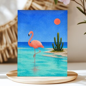 May include: A rectangular art print featuring a vibrant pink flamingo standing on one leg in shallow turquoise water. A green cactus grows on a sandy shore nearby under a bright blue sky with a solid orange circular sun positioned in the upper right.