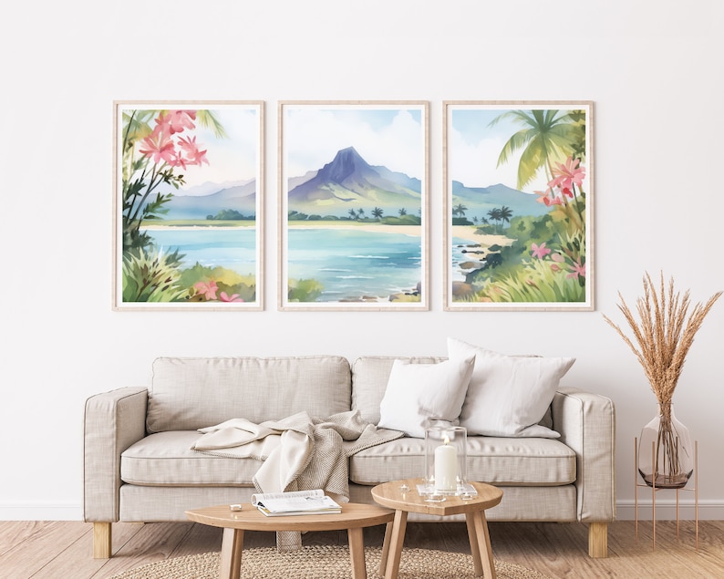 May include: A set of three framed watercolour prints depicting a tropical coastal landscape with a central mountain, blue water, sandy beaches, and pink flowers in the foreground. The artwork features light blue, green, and soft pink colour tones.