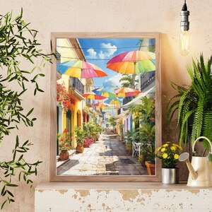 May include: A watercolour painting of a colourful street scene with umbrellas hanging over a cobbled street. The umbrellas are red, yellow, blue, green and purple. The buildings are yellow and have green plants growing on them.