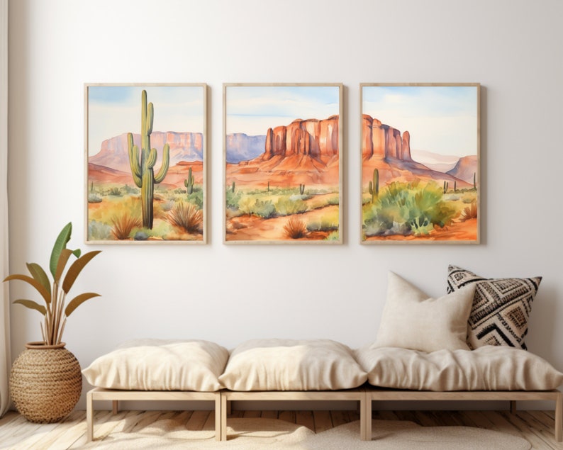 May include: A set of three framed watercolour prints depicting a desert landscape with saguaro cacti, red rock mesas, and sparse vegetation under a pale blue sky. The artwork features warm orange, red, and green tones, presented in light wood frames.