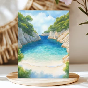May include: Watercolor painting of a serene coastal scene. Turquoise water flows between white cliffs, leading to a sandy beach. Lush green trees and a blue sky with fluffy clouds complete the landscape. The artwork is displayed on a wooden stand.
