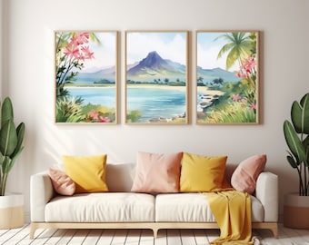 Pode incluir: Um tríptico de impressões em aguarela emolduradas que retratam uma paisagem costeira tropical com uma montanha central, água turquesa, praias de areia e flores cor-de-rosa. A obra está exposta sobre um sofá branco com almofadas amarelas e rosas.