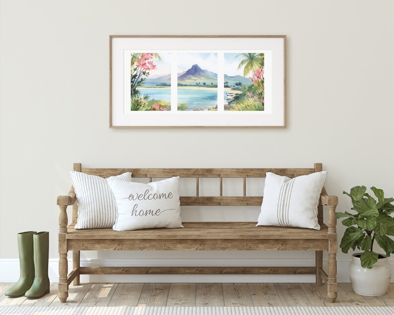 May include: A framed triptych watercolour print depicting a tropical coastal landscape with a central mountain, blue water, and lush foliage. The artwork is displayed above a wooden bench featuring two white pillows with the text welcome home.