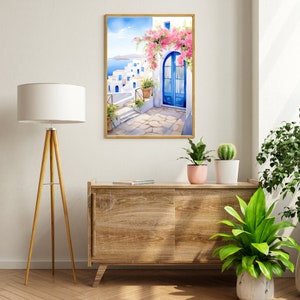 May include: A framed wall art print depicting a Mediterranean coastal scene with white buildings, blue doors, and vibrant pink bougainvillea flowers. The artwork features a stone patio, potted plants, and a distant view of the blue sea under a clear sky.