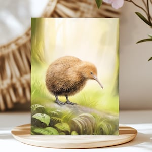 May include: A greeting card featuring a detailed illustration of a kiwi bird standing on a log in a forest setting. The kiwi has brown feathers and a long beak. The background is a soft, blurred depiction of trees and foliage.
