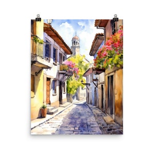 May include: A watercolor painting of a narrow, cobblestone street in a European village. The street is lined with white buildings with terracotta roofs and balconies adorned with pink flowers. A church tower rises above the buildings in the distance.