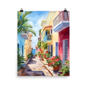 May include: A watercolour print depicting a narrow street lined with colourful buildings in shades of blue, yellow, and red. Potted plants with pink flowers sit along the path, and a palm tree stands on the left. The street leads towards the sea.