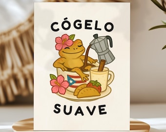 May include: A rectangular greeting card featuring a yellow frog relaxing in a cup decorated with a Puerto Rican flag. The frog wears a pink hibiscus flower and pours coffee from a moka pot. Beside the cup are two empanadas and a mug.