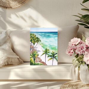 Puede incluir: Pintura a la acuarela de una escena de playa tropical. La obra de arte representa una playa de arena blanca, agua turquesa y exuberantes palmeras verdes. El cielo es de un azul claro. La pintura se exhibe sobre una superficie blanca.