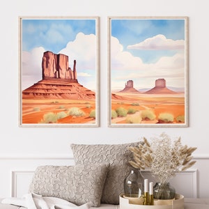 May include: Two framed vertical wall art prints depicting Monument Valley landscapes. The left print shows a large red sandstone butte, while the right print features two smaller buttes in a desert setting with blue skies and white clouds.