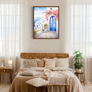 May include: A framed wall art print depicting a Mediterranean coastal scene with white buildings, a bright blue arched door, and vibrant pink bougainvillea flowers. The artwork features a stone patio, potted plants, and a view of the blue sea.