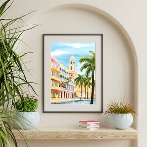 Peut inclure: Une impression encadr&eacute;e d'une ville color&eacute;e avec un immeuble haut et des palmiers. Les b&acirc;timents sont peints dans des tons de jaune, rose et bleu. Les palmiers sont verts et ont une ambiance tropicale.