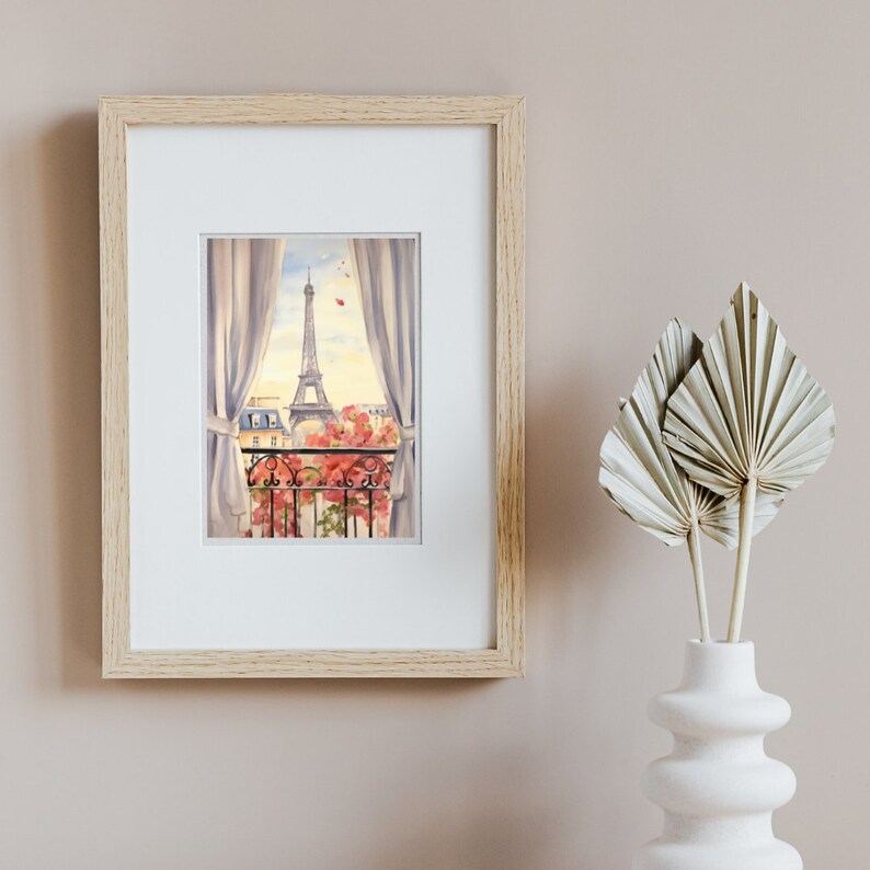 May include: A framed watercolor print featuring a view from a balcony looking toward the Eiffel Tower in Paris. The scene includes white curtains, a black wrought iron railing, and pink flowers, all encased in a light-colored wooden frame.