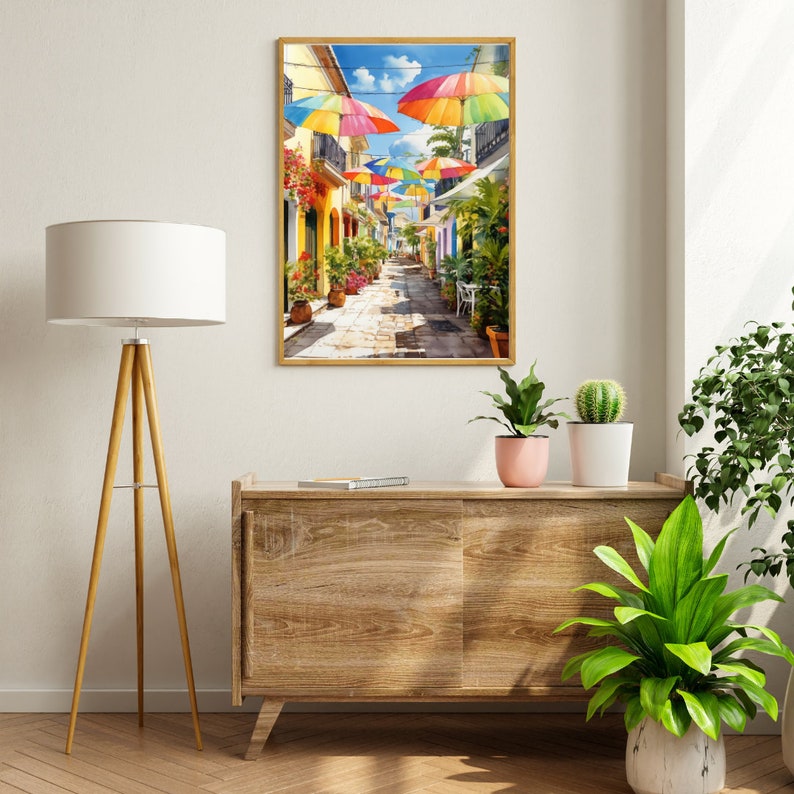 May include: A colourful painting of a narrow street lined with buildings and colourful umbrellas overhead. The street is paved with cobblestones and there are plants and flowers in pots along the sides of the street.