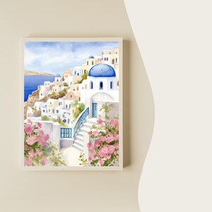 Puede incluir: Una pintura en acuarela enmarcada que representa un pueblo costero con edificios blancos, techos de c&uacute;pula azul y escaleras de piedra. La escena incluye flores de buganvilla rosa vibrantes en primer plano y el mar azul profundo.