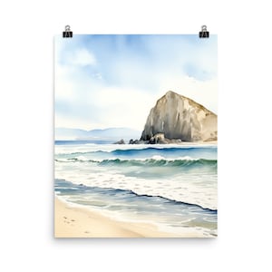 May include: A watercolor art print depicting a coastal scene with a large, tan rock formation rising from the ocean. The composition features rolling blue and green waves washing onto a light beige sandy beach under a soft, pale blue sky.