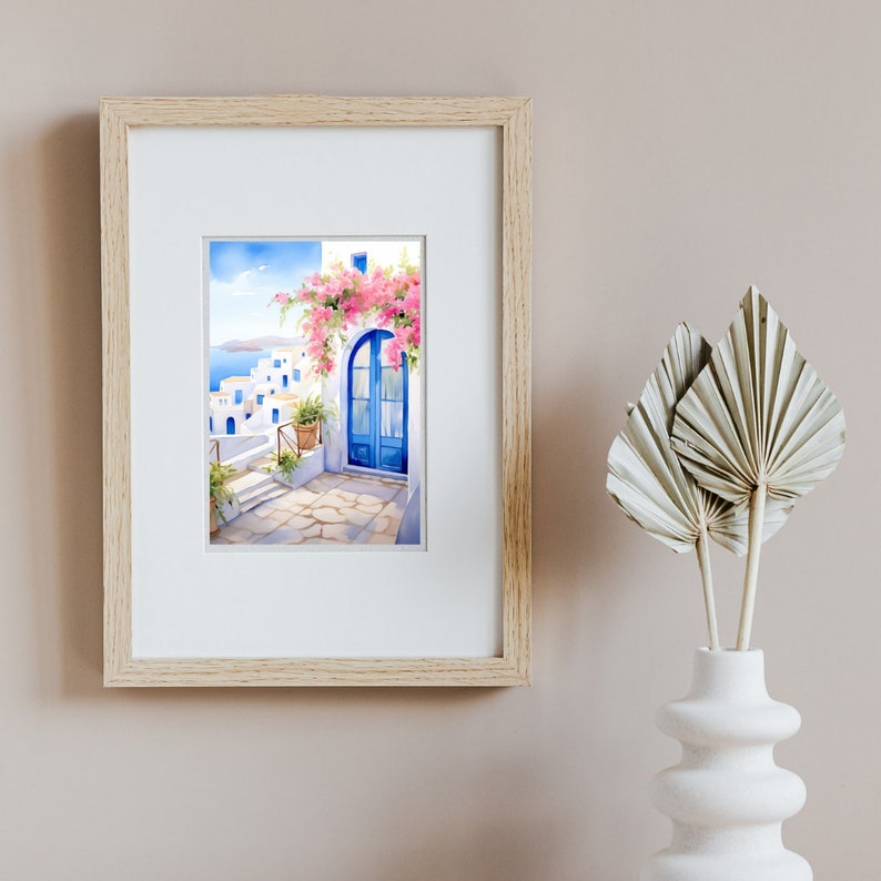 May include: A framed watercolor print depicting a Mediterranean scene with white buildings, a bright blue arched door, and vibrant pink bougainvillea flowers. The artwork is displayed in a light wood frame with a white mat, showcasing a coastal view.