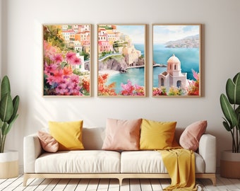 May include: A set of three framed wall art prints featuring watercolor illustrations of a coastal Mediterranean village. The images depict colorful hillside buildings, vibrant pink bougainvillea flowers, a blue sea, and a white domed church.