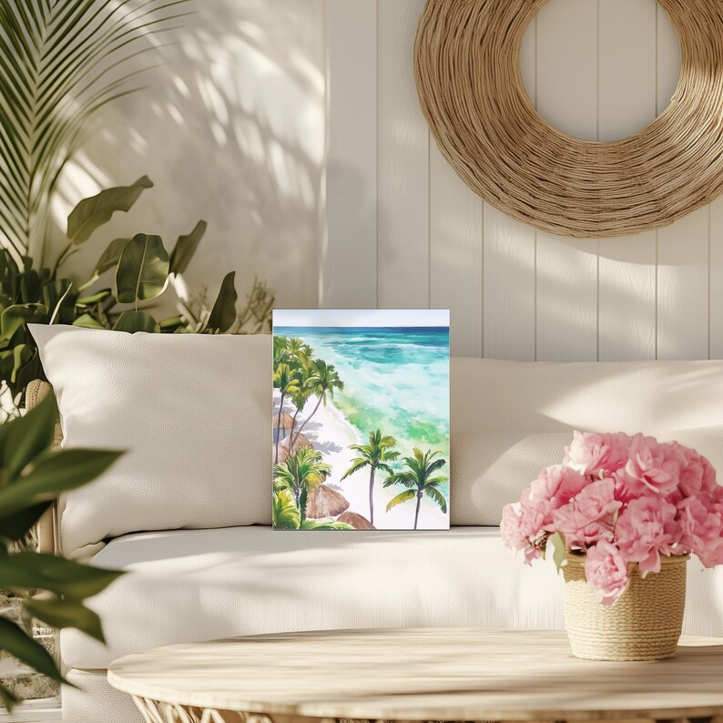 Puede incluir: Pintura a la acuarela de una escena de playa tropical con palmeras, arena blanca y agua turquesa. La obra de arte se exhibe en un sof&aacute; blanco con una decoraci&oacute;n de pared circular tejida y una cesta de flores rosas.