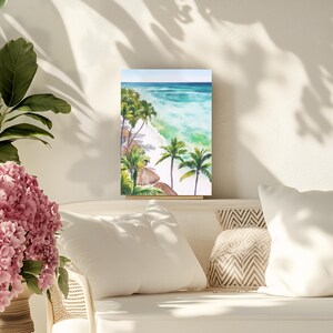 Puede incluir: Pintura a la acuarela de una escena de playa tropical. La obra de arte representa una playa de arena blanca, agua turquesa y exuberantes palmeras verdes. El cielo es de color azul claro. La pintura se exhibe sobre una superficie blanca.