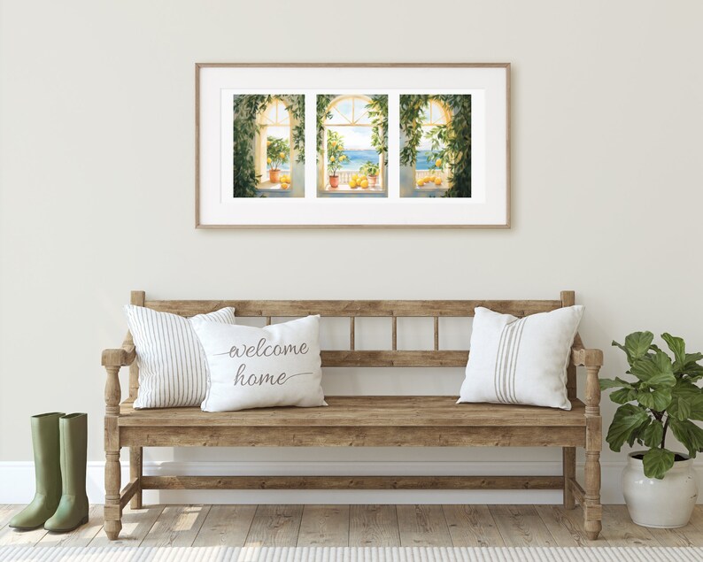May include: A wooden bench with two pillows, one with the text "welcome home" and the other with white and gray stripes. A green plant in a white pot is on the right side of the bench. A framed print of three windows with a view of the ocean and lemon trees is hanging on the wall behind the bench.