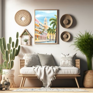 Peut inclure: Une peinture &agrave; l'aquarelle encadr&eacute;e repr&eacute;sentant une sc&egrave;ne de rue color&eacute;e avec des palmiers et un immeuble haut. La peinture est accroch&eacute;e &agrave; un mur blanc au-dessus d'un canap&eacute; clair avec des coussins et une couverture.