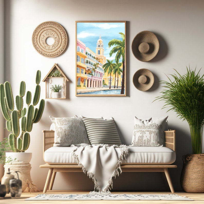 Peut inclure: Une peinture &agrave; l'aquarelle encadr&eacute;e repr&eacute;sentant une sc&egrave;ne de rue color&eacute;e avec des palmiers et un immeuble haut. La peinture est accroch&eacute;e &agrave; un mur blanc au-dessus d'un canap&eacute; clair avec des coussins et une couverture.