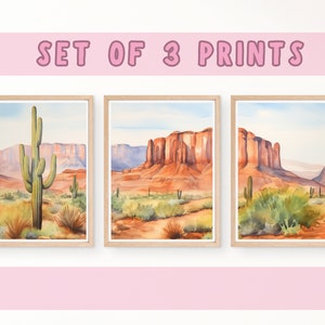 May include: A set of three framed watercolour prints featuring desert landscapes with saguaro cacti, red rock formations, and sparse vegetation under a pale blue sky. The text SET OF 3 PRINTS is displayed in pink letters above the framed artwork.