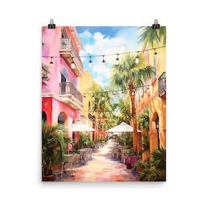 May include: A vertical art print depicting a sunlit street scene with pink and yellow buildings, palm trees, and outdoor cafe seating under white umbrellas. Strings of lights hang across the walkway, and the sky is bright blue with clouds.