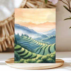 May include: Watercolor painting of a landscape featuring terraced rice fields and rolling hills. The artwork showcases a gradient sky with orange and yellow hues, transitioning to blue mountains and green fields. The painting is displayed on a wooden tray.