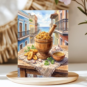 May include: A watercolor illustration of a wooden mortar and pestle filled with mofongo, accompanied by fried plantain slices, garlic cloves, and a small bowl of broth on a textured cloth, set against a backdrop of colorful colonial buildings.