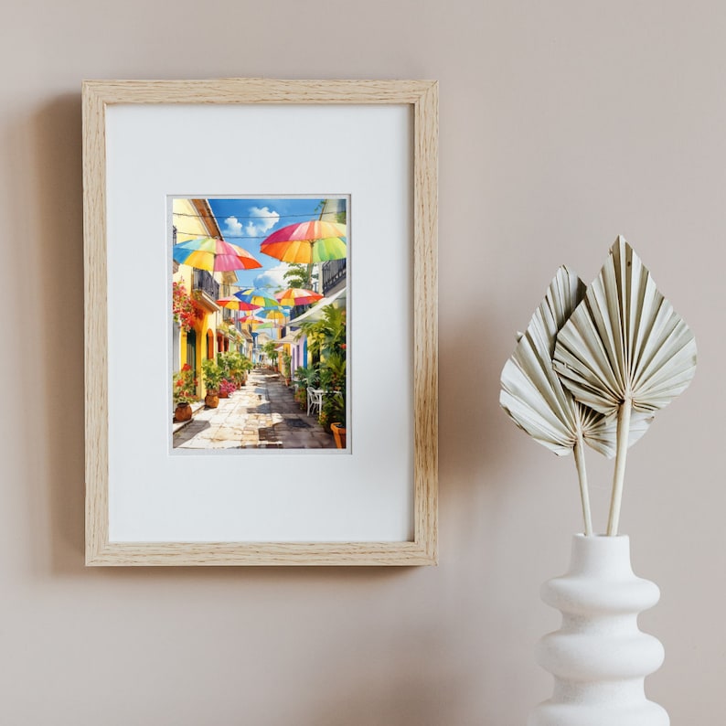 May include: A framed print of a colourful street scene with rainbow umbrellas hanging over a narrow cobbled street lined with colourful buildings.
